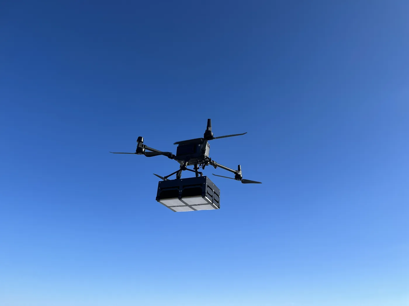 Northern Drone survey drone carrying a GPR payload, seen from below against a clear blue sky