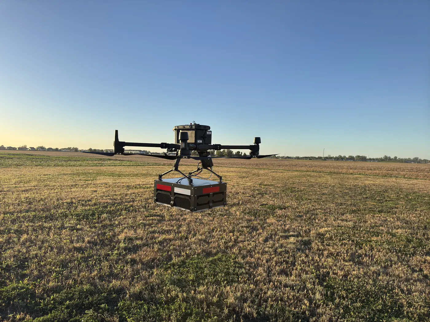 Northern Drone survey drone with GPR payload hovering over a harvested North Dakota field at sunrise