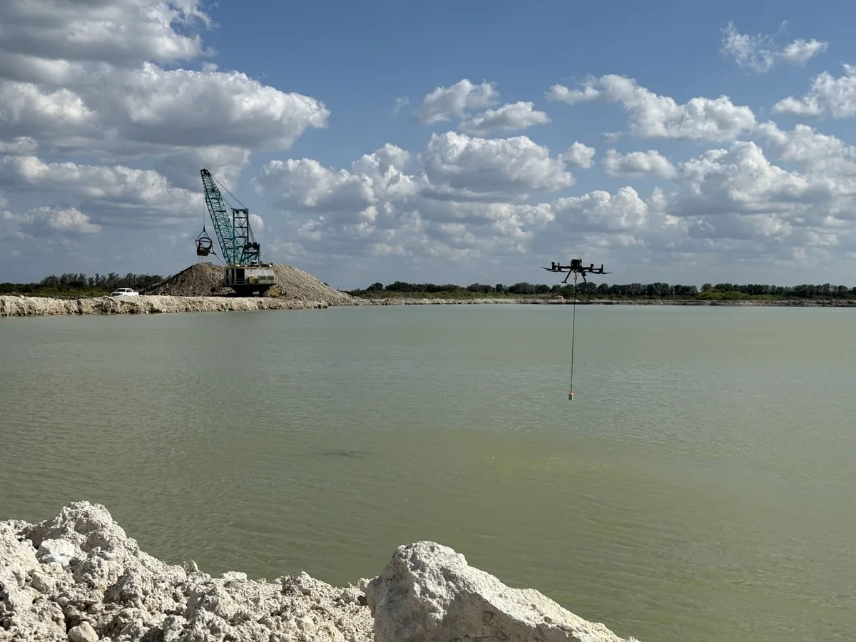 DJI M300 RTK flying a tethered sonar sensor over a flooded aggregate quarry pit, dragline excavator working the bank behind