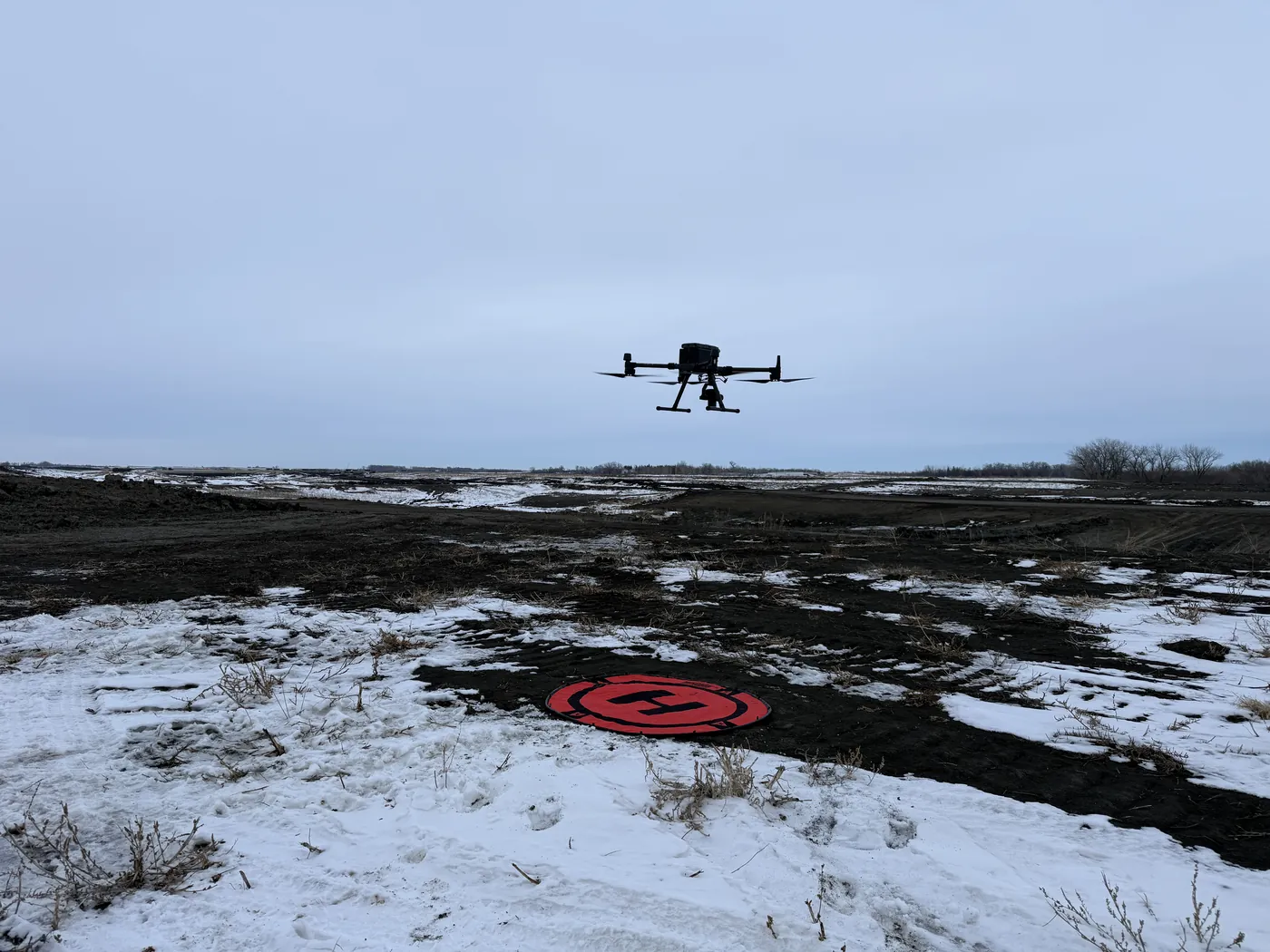 Northern Drone survey drone flying over snow and frozen mud with the landing pad below